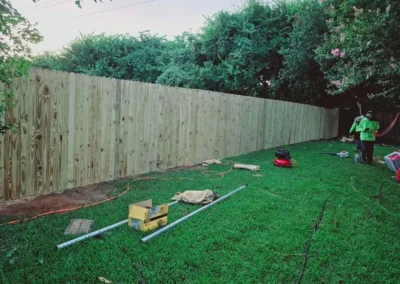 A wooden fence surrounds a green grassy area, with various gardening tools placed nearby